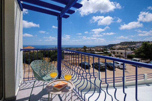 A balcony with a view of the sea, a blue railing, and a table with a book and drinks.