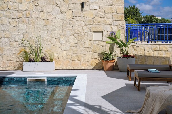 A stone wall, a swimming pool, potted plants, and lounge chairs.