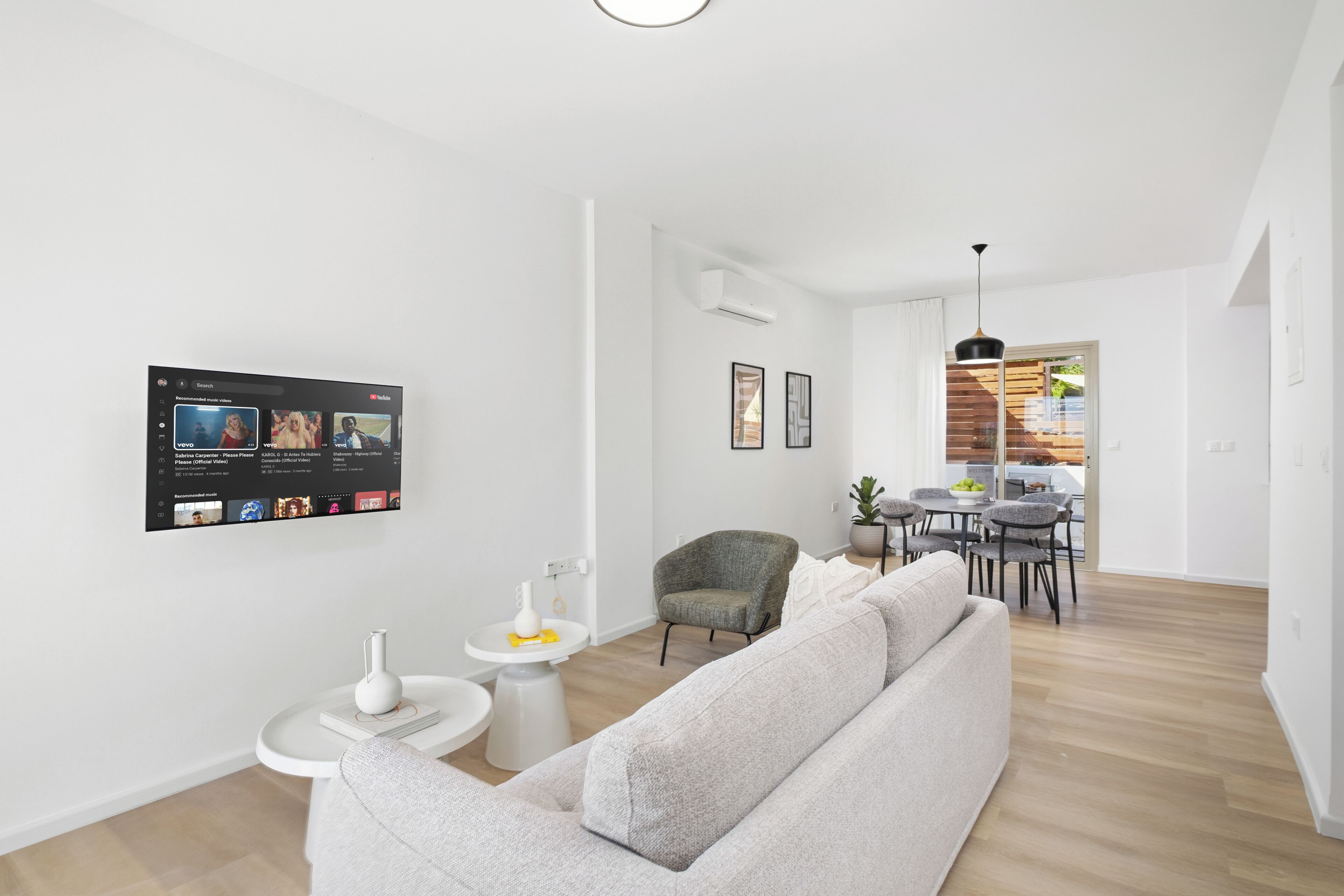Ein modernes Wohnzimmer mit einer Couch, einem kleinen Tisch, einem Sessel und einem montierten Fernseher, der eine Streaming-Dienstanwendung zeigt.