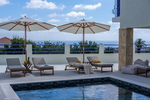 A poolside area with lounge chairs, umbrellas, and a view of the sea.