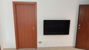 Een kamer met een houten deur, een tv aan de muur en een betegelde vloer.