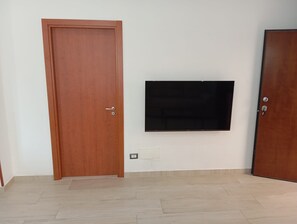 Une pièce avec une porte en bois, un téléviseur fixé au mur et un sol carrelé.