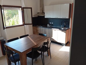 Une cuisine de taille réduite, avec une table et des chaises en bois, une fenêtre avec des rideaux et des armoires blanches.