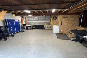 A spacious basement with a kitchen area, a dartboard, and a white refrigerator.