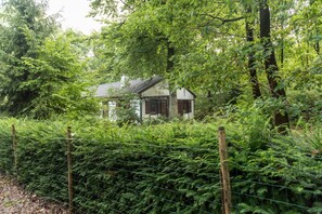 A small, traditional house surrounded by dense greenery and a wire fence.