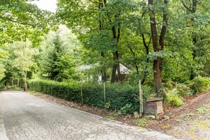 A paved road flanked by dense greenery and a white building with a dark roof.