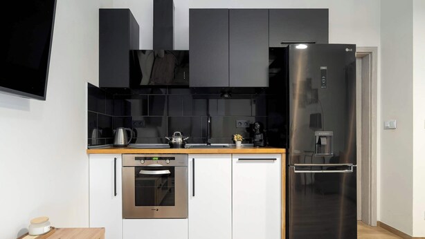 Una cocina moderna con refrigerador, horno y lavavajillas de acero inoxidable, cubierta de madera y gabinetes negros.