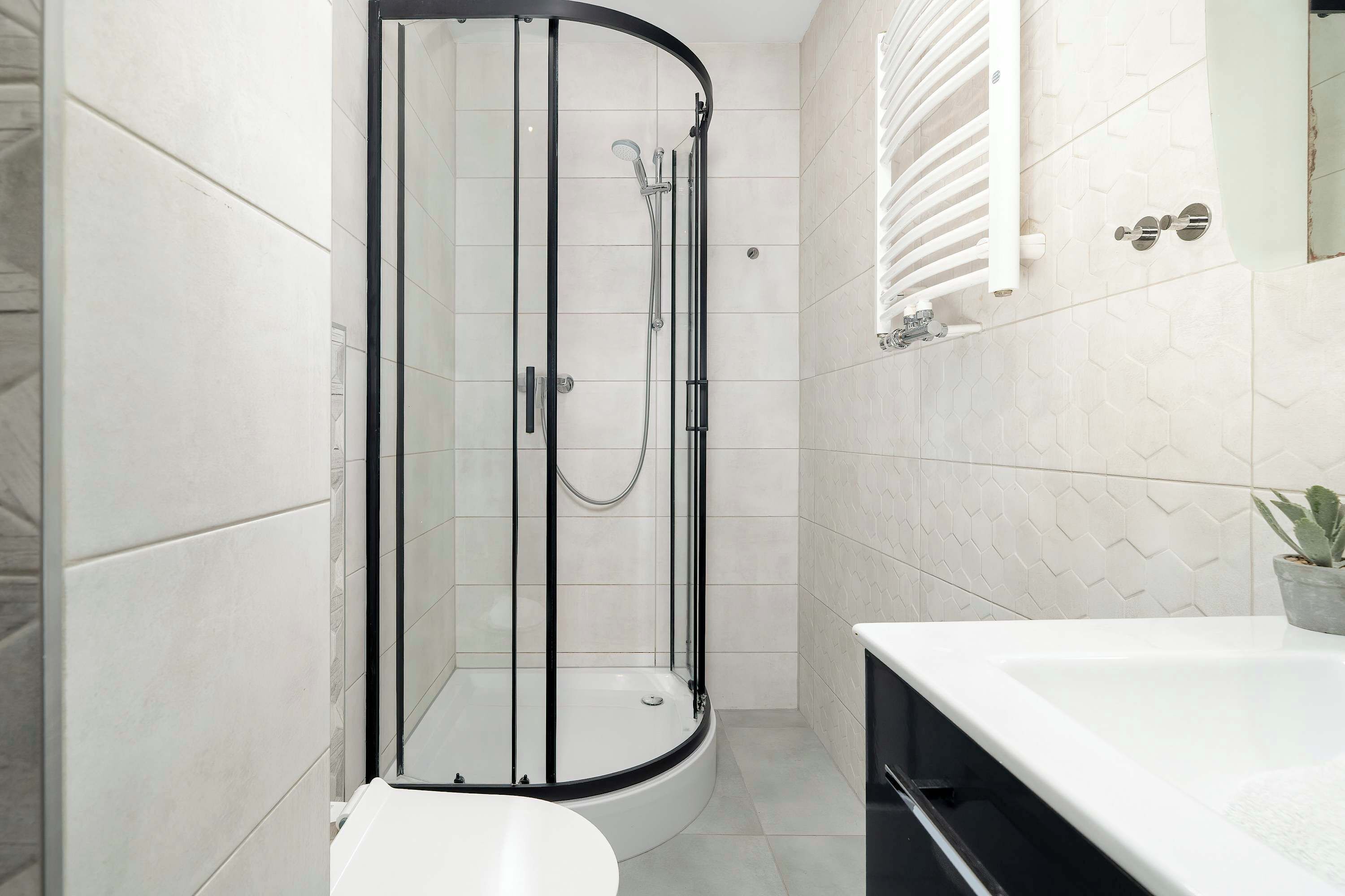 A modern bathroom with a glass-enclosed shower, a white bathtub, and a potted plant.