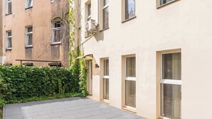 Un patio con suelo de baldosas, un seto y un edificio con varias ventanas y una puerta.