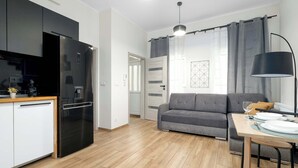 Una cocina moderna con un refrigerador negro, un comedor con mesa y sillas, un sofá gris y un ventanal con cortinas.