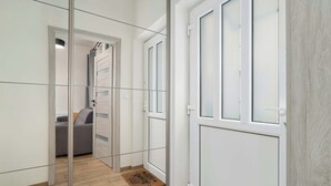 Un pasillo con un separador de vidrio, piso de madera, una puerta blanca y un sofá gris al fondo.
