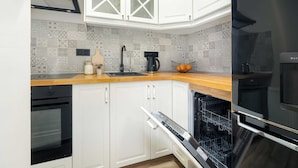 A kitchen with white cabinets, a black oven, a dishwasher, and a coffee maker. - A Comfortable Apartment in the Centre of Poznań | Close to the MTP (Poznań)