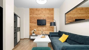 A modern living room with a wooden wall panel, a flat-screen TV, a dark green sofa, a white coffee table, and a mirror. - A Comfortable Apartment in the Centre of Poznań | Close to the MTP (Poznań)