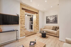 Un salon moderne avec un mur d’accent en pierre, un téléviseur à écran plat, un canapé, une table basse et un tableau encadré représentant un paysage urbain.