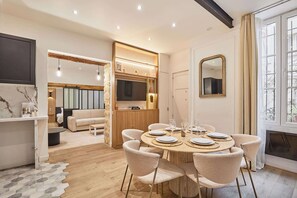 Un espace repas moderne avec une table ronde prévue pour quatre personnes, entourée de six chaises. Un téléviseur est fixé au mur au-dessus de l’espace détente.