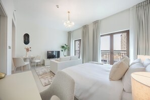 Habitación de hotel con cama, escritorio, silla, televisor y balcón con vistas.