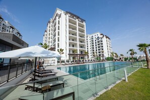 A poolside area with lounge chairs and umbrellas, surrounded by high-rise buildings. - Bloomfields Studio in Albatross 2 - YGC  (Abu Dhabi)