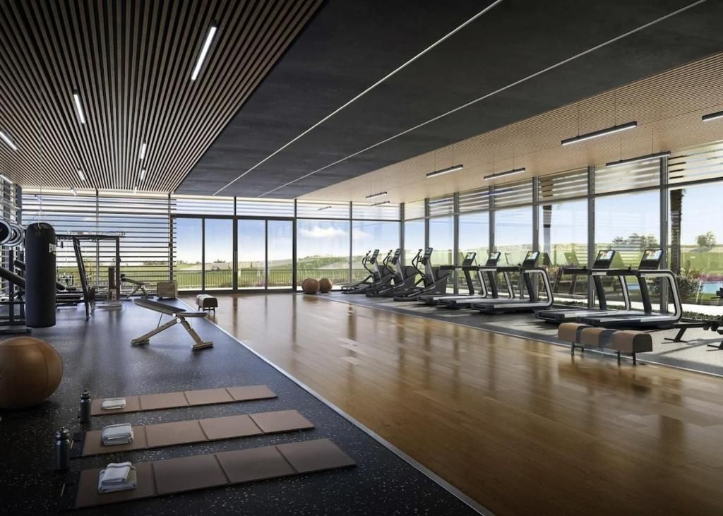 Een sportschool met trainingsapparatuur, grote ramen en een houten vloer.