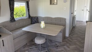 A compact living space with a sofa, a small table, a mirror, and an air conditioning unit. - De Zeeuwse Parel Vacation Park - Sunset Comfort (Scherpenisse)