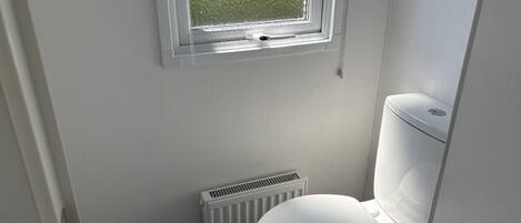 Un baño pequeño y limpio con inodoro blanco, un radiador y una ventana que da a zonas verdes.