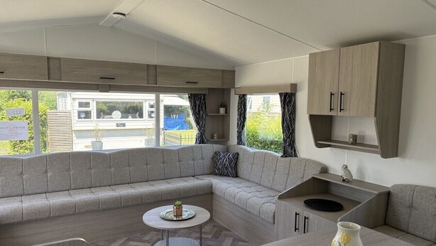 A modern RV interior with a sectional sofa, a round table, and a kitchenette area. - De Zeeuwse Parel Vacation Park - Sunset Comfort (Scherpenisse)