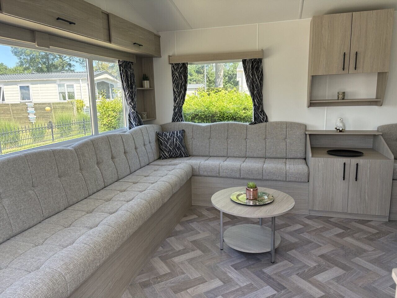 Un interior moderno de autocaravana con sofá modular, una pequeña mesa de comedor y una kitchenette.