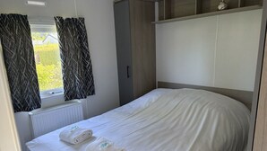 A single bed with white linens, a radiator, a wardrobe, and a window with curtains. - De Zeeuwse Parel Vacation Park - Sunset Comfort (Scherpenisse)