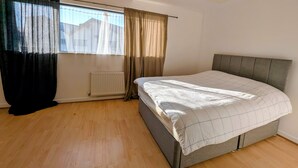 A bedroom with a bed, a window with curtains, a radiator, and a ceiling light. - Modern 2BDR Garden Home With Parking and WiFi (Greater London)