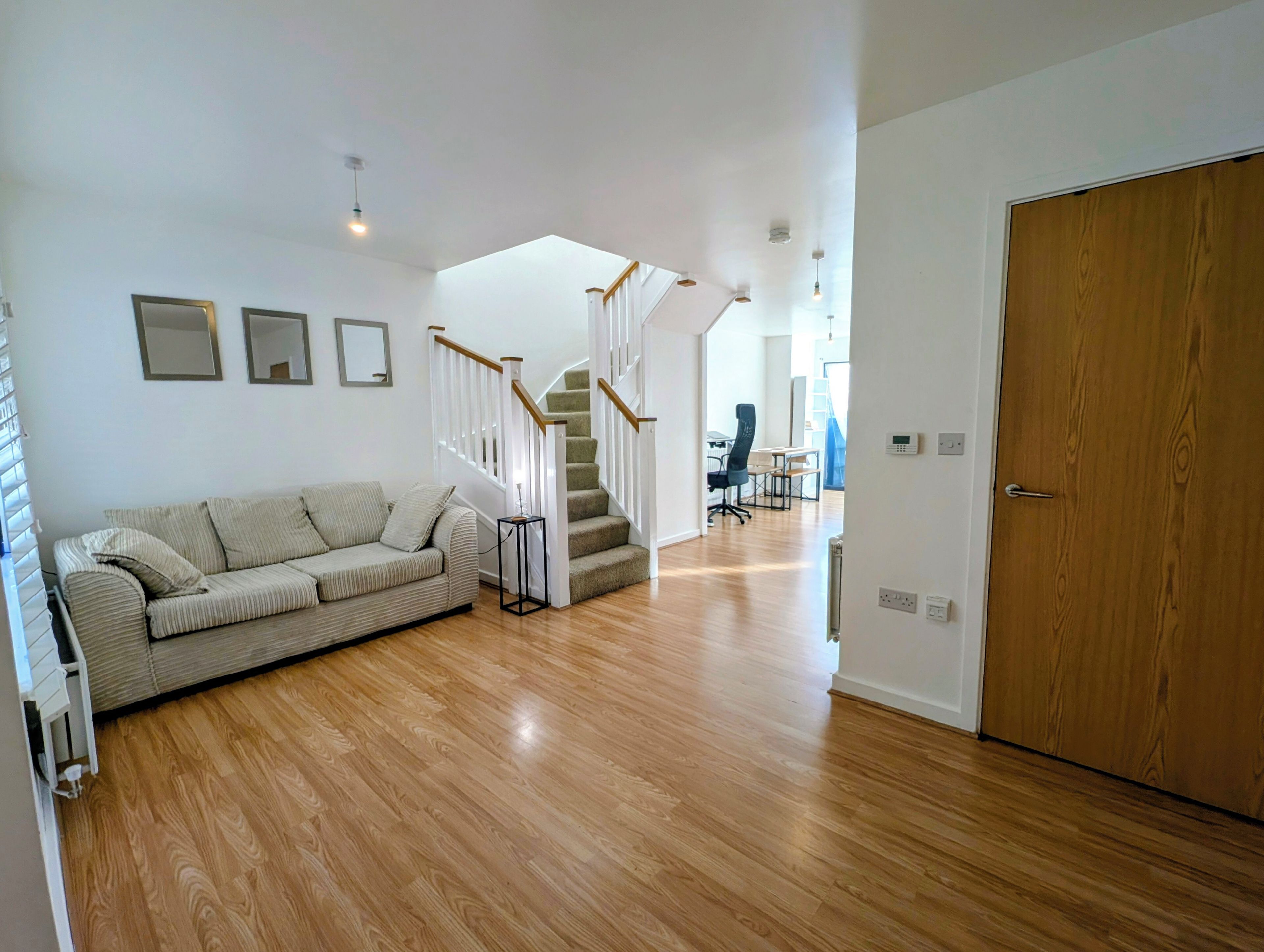 Uma sala de estar moderna com piso de madeira, um sofá, uma escada e uma porta.