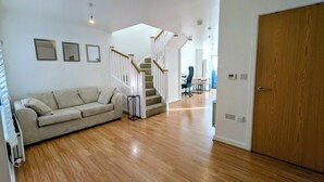 A modern living room with a wooden floor, a sofa, a staircase, and a door. - Modern 2BDR Garden Home With Parking and WiFi (Greater London)
