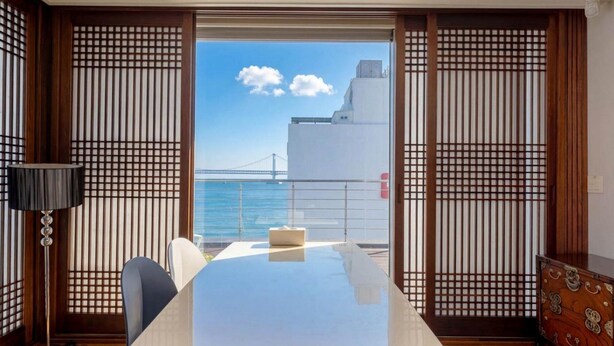 A room with a large table, chairs, a lamp, and a view of a bridge and water. - Busan LaMer Gwangan Stay (Busan)