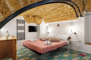 A bedroom with a stone ceiling, a bed with a pink bedspread, a wooden dresser, and a colorful tiled floor. - Suite Radici  Holiday Home: Elegance and Tradition in the Heart of Palermo (Palermo)