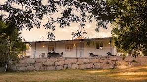 Una casa de dos pisos con un muro de piedra al frente, un patio con mobiliario exterior y un cielo despejado.