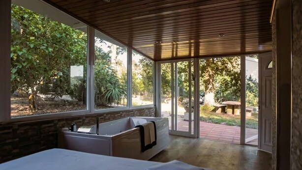 Un dormitorio con una cama grande, una zona de estar con un banco, una bañera y vistas al exterior.
