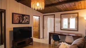 Una sala de estar con televisor, muebles de madera, una araña y una puerta que da a otra habitación.