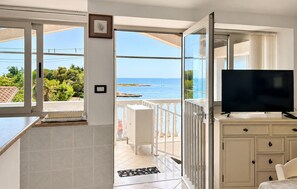 Een kamer met een televisie, een balkon en uitzicht op zee, en een deur naar een buitengebied.