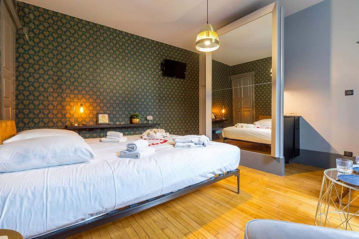 Um quarto com uma cama, uma mesa de cabeceira, uma luminária, um espelho e uma pequena mesa redonda com um copo.