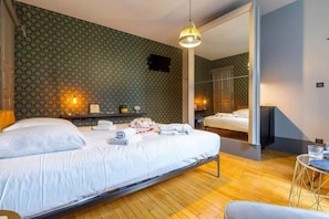 Um quarto com uma cama, uma mesa de cabeceira, uma luminária, um espelho e uma pequena mesa redonda com um copo.