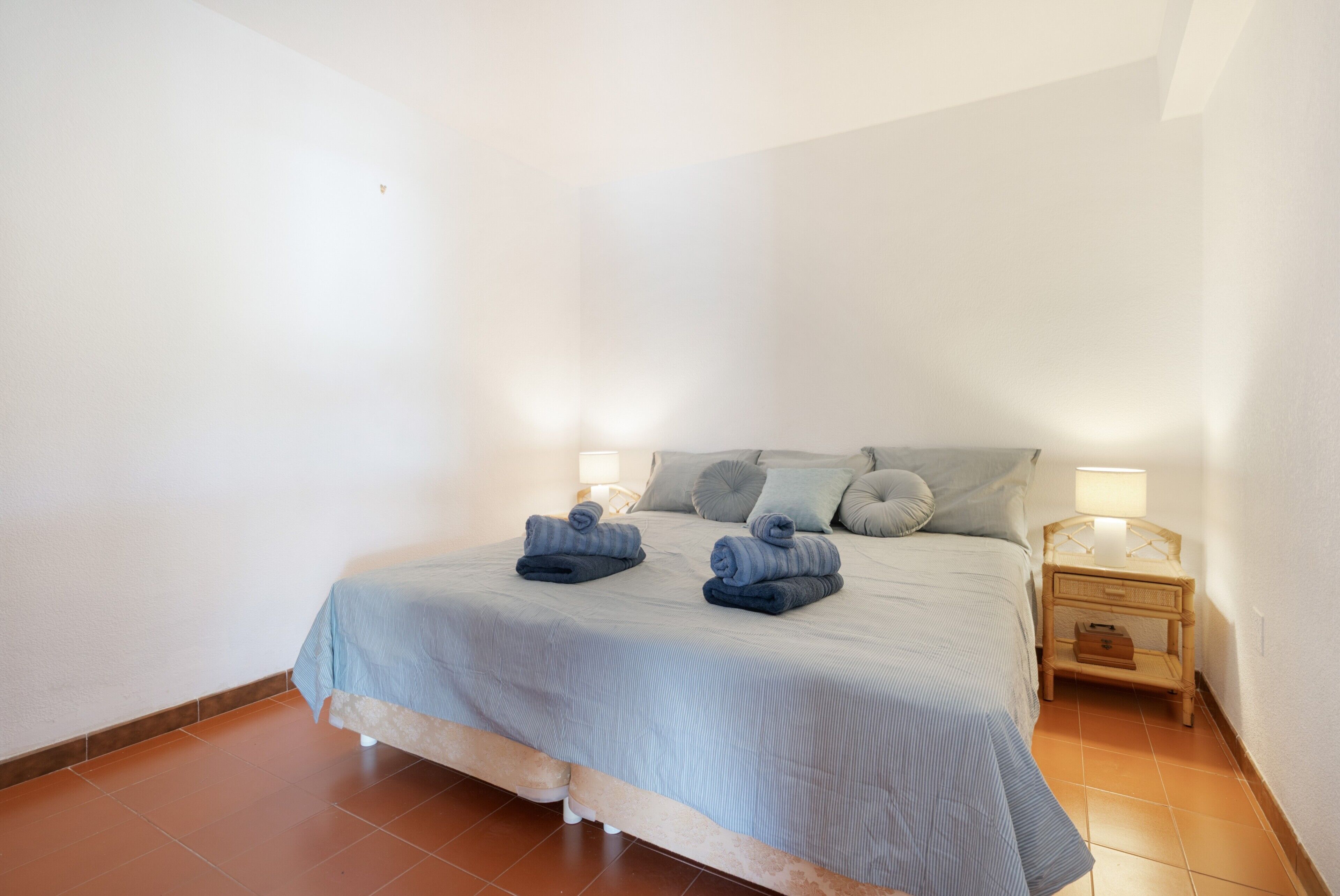 A bedroom with a bed, pillows, a nightstand, and a lamp.