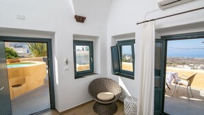 Ein Zimmer mit einem runden Korbstuhl, einem kleinen Tisch und Meerblick durch ein Fenster.