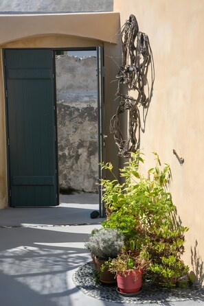 Entrada d'un edifici amb una porta verda, una escultura penjada a la paret i plantes en testos.