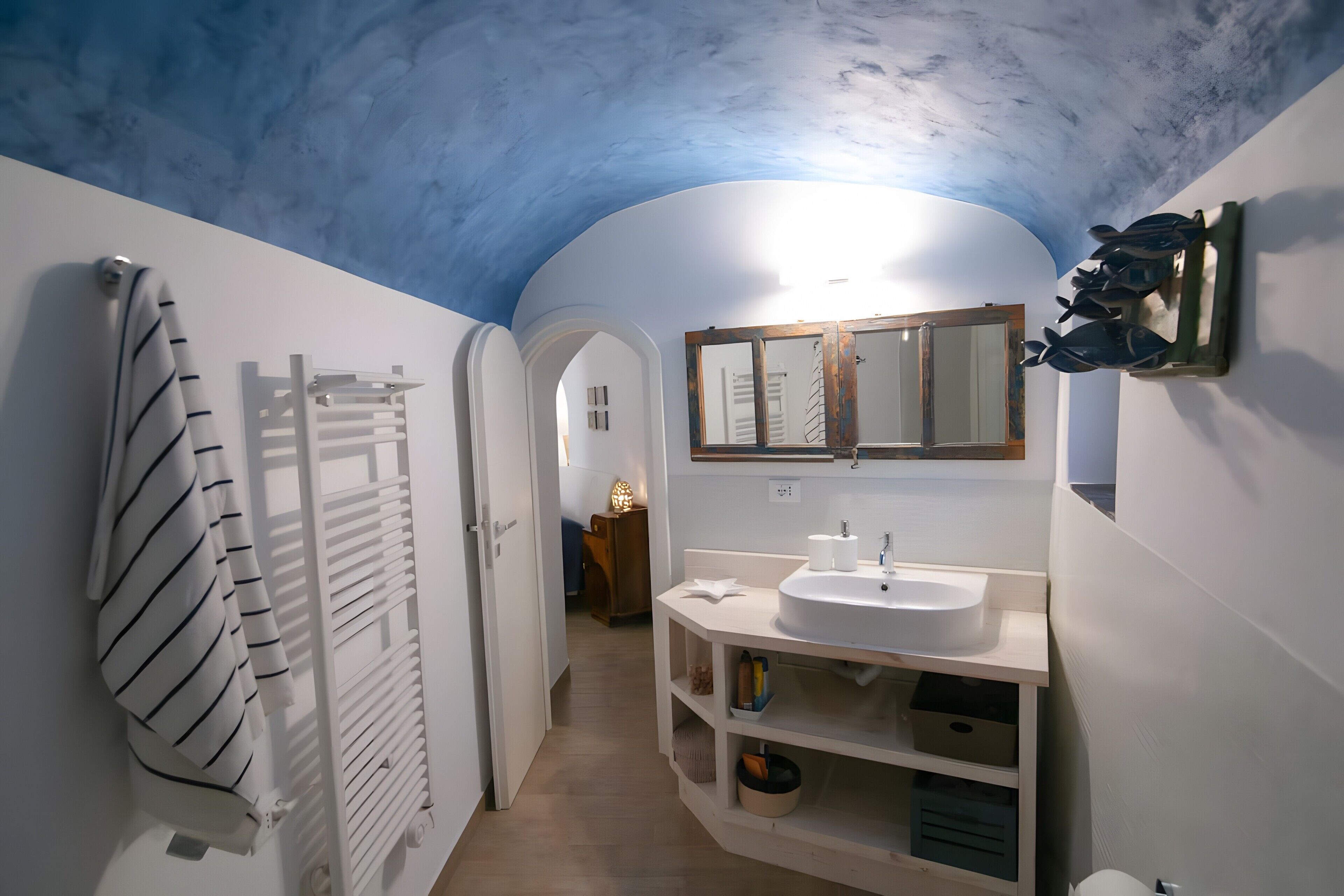 A bathroom with a white vanity, a mirror, a towel rack, and a ceiling with a blue hue.