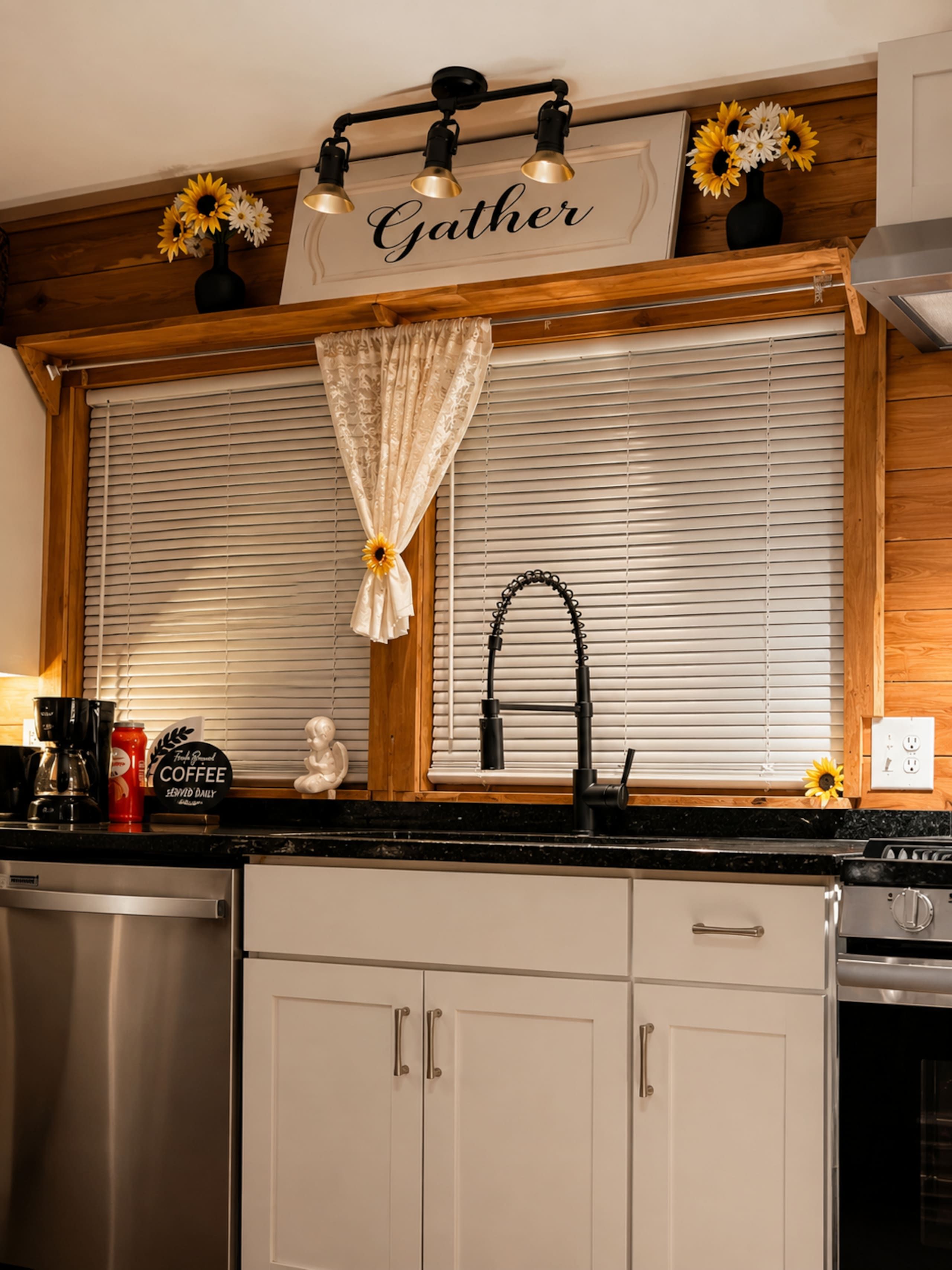 Una cocina con lavavajillas de acero inoxidable, cafetera y un cartel que dice 'Gather'.
