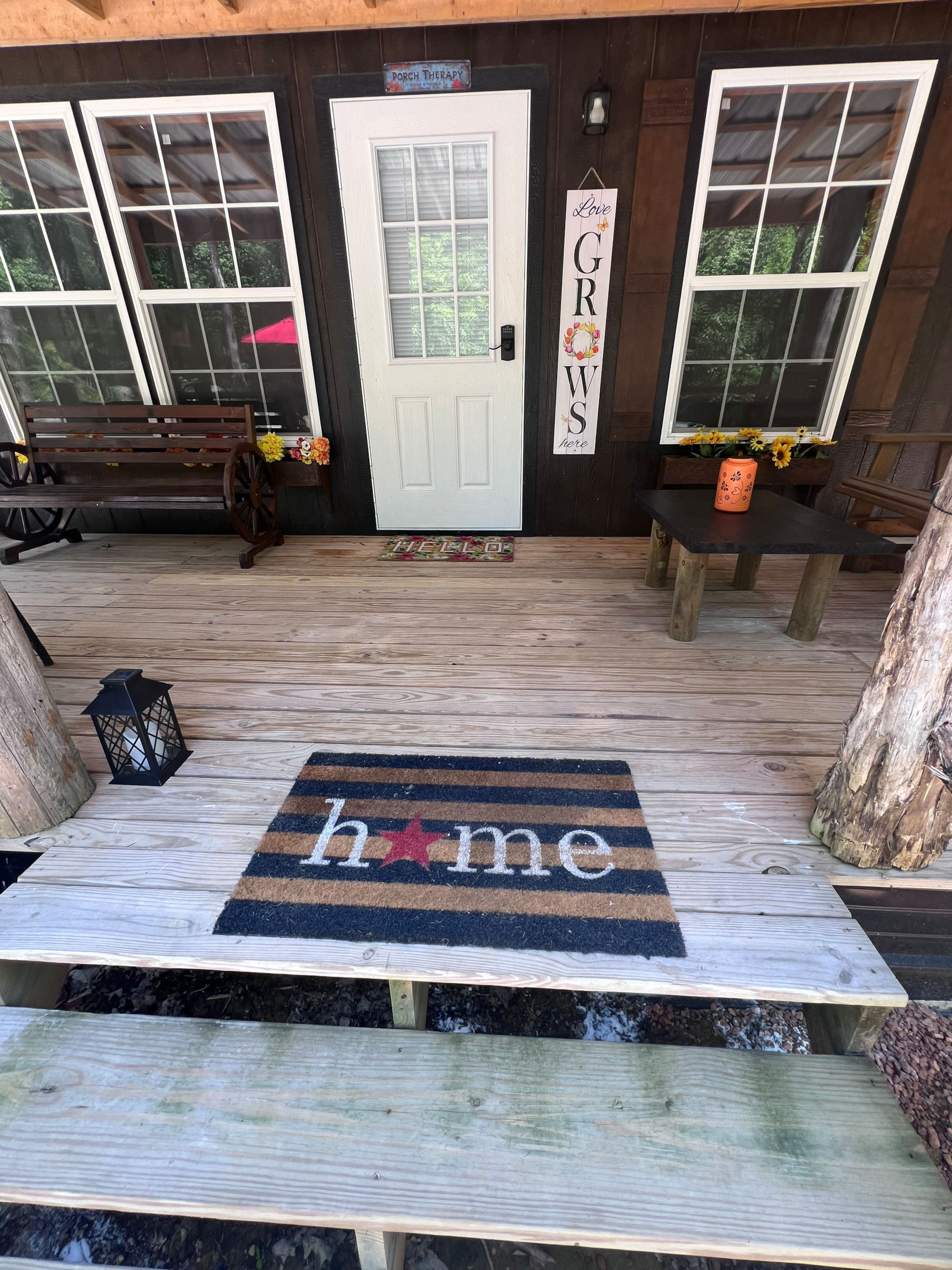 A wooden porch with a bench, a welcome mat, and a door with a sign.