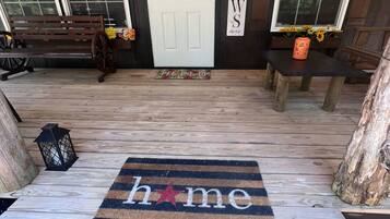A wooden porch with a bench, a welcome mat, and a door with a sign.