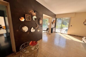 A spacious room with a dark wall adorned with various mirrors and wall art, a large window with a view of greenery, and a tiled floor. - Grand French Family Holiday Home (Saint-Germain sur Bresle)