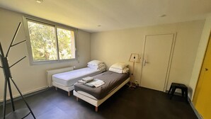 Une chambre à coucher avec un lit, une fenêtre, un radiateur, une porte et un petit tabouret.