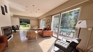 Un salon spacieux avec une cheminée, un canapé, une table basse et un téléviseur. De grandes fenêtres offrent une vue sur l’extérieur.