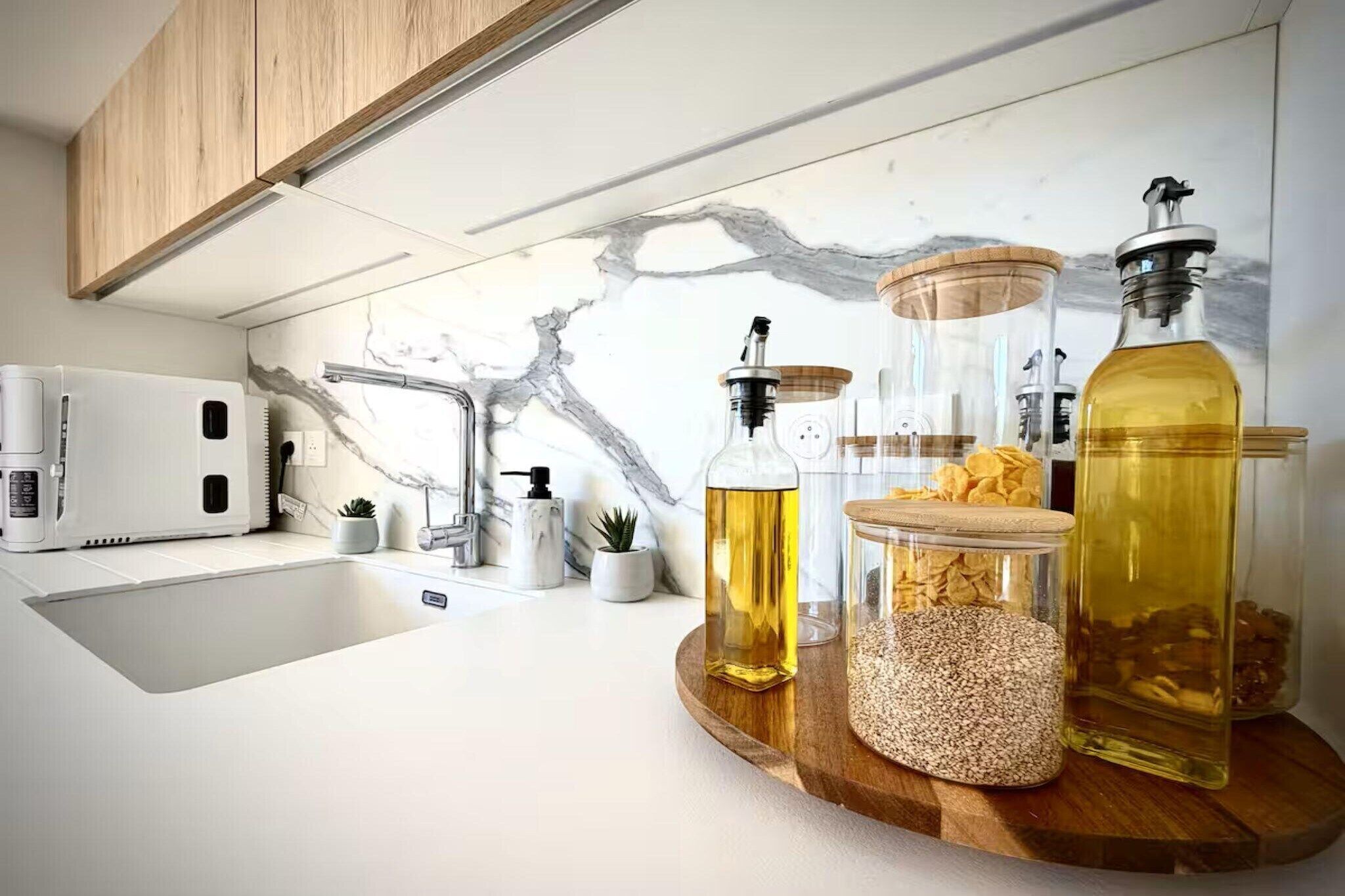 A kitchen with a modern design, featuring a white countertop, a built-in coffee machine, and various kitchen utensils.
