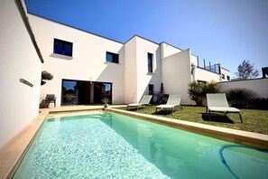 Une maison moderne dotée d’une piscine, de chaises longues et d’une pelouse bien entretenue.